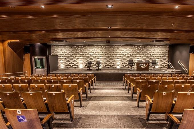 Auditório com revestimento acústico em madeira e assentos escalonados
